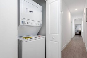 Une buanderie équipée d’un lave-linge et d’un sèche-linge à chargement frontal, d’une porte et d’un couloir menant à une autre pièce.
