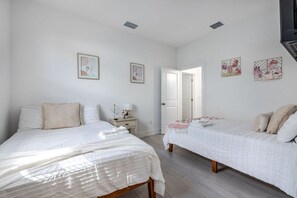 Ein Schlafzimmer mit zwei Betten, einem Nachttisch mit Lampe und einer Tür zu einem weiteren Raum.