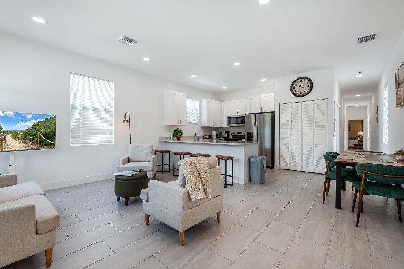 A modern kitchen with white cabinets, a stainless steel refrigerator, and a dining area with green chairs.