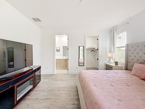 Ein Schlafzimmer mit Fernseher, Bett, Nachttisch und Fenster.