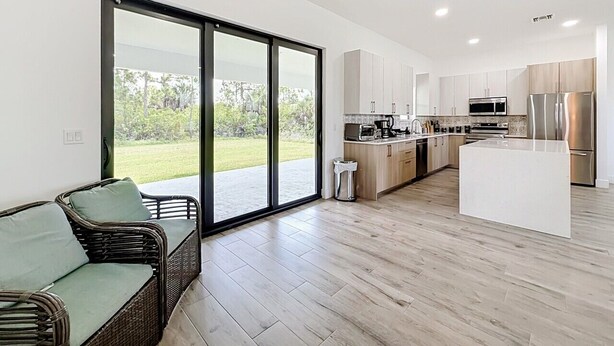 A modern kitchen with a central island, sliding glass doors leading to a garden, and a wicker sofa. - Cozy Retreat in Port Charlotte (Port Charlotte)
