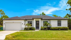 Einbungalow mit Garage, Eingangstür und kleinem Vorgarten mit Rasen und einigen Bäumen.