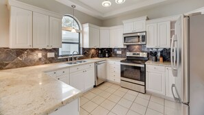 A modern kitchen with white cabinets, a granite countertop, a built-in oven, and a stainless steel refrigerator. - Gun Barrel Lakefront Retreat (Gun Barrel City)