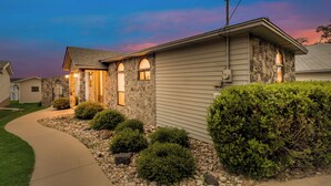 A two-story house with a stone facade, a curved driveway, and a well-maintained front yard with bushes and a small tree. - Gun Barrel Lakefront Retreat (Gun Barrel City)
