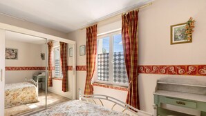 Ein Schlafzimmer mit einem Bett, einem Schreibtisch, einem Spiegel und einem Fenster mit Vorhängen.