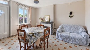 Ein Essbereich mit Tisch und Stühlen, einer Couch, einem Fenster mit Vorhängen und einem Wandspiegel.