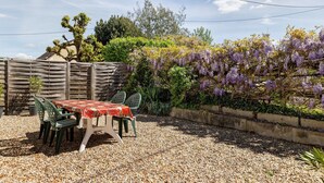 Eine Terrasse im Freien mit Tisch und Stühlen, umgeben von Kies und Pflanzen.