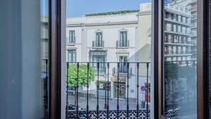 A view through a window with a balcony, featuring a building with a shop on the ground floor, a no parking sign, and a tree. - Suite Torre del Oro Seville: Pool, Balcony & AC in El Arenal (Sevilla)