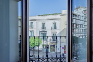 A view through a window with a balcony, featuring a building with a shop on the ground floor, a no parking sign, and a tree. - Suite Torre del Oro Seville: Pool, Balcony & AC in El Arenal (Sevilla)