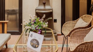 A lobby with wicker chairs, a glass table with a sign, and a decorative fountain. - Suite Torre del Oro Seville: Pool, Balcony & AC in El Arenal (Sevilla)