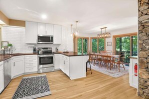 Una cocina moderna con armarios blancos, electrodomésticos de acero inoxidable y una zona de comedor con muebles de madera.