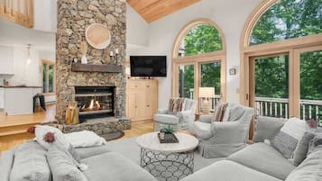 A spacious living room with a stone fireplace, comfortable seating, and large windows offering a view of the outdoors.