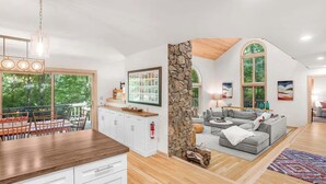 Ein geräumiger Wohnbereich mit einer Wand aus Naturstein, einem grauen Sofa und einem Essbereich mit Holzschränken und einem großen Fenster.