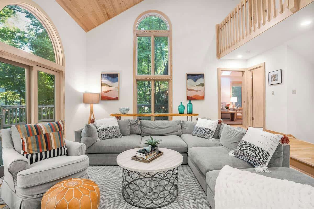 A modern living room with a large window, a sofa set, a coffee table, and a staircase.