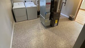 Un cuarto de lavandería con dos lavadoras y una secadora, piso alfombrado y conductos visibles.