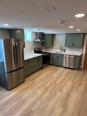 A modern kitchen with stainless steel appliances, light green cabinets, and a wooden floor.