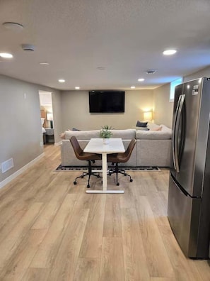 A modern kitchen with a dining table, chairs, a refrigerator, and a flat-screen TV mounted on the wall.
