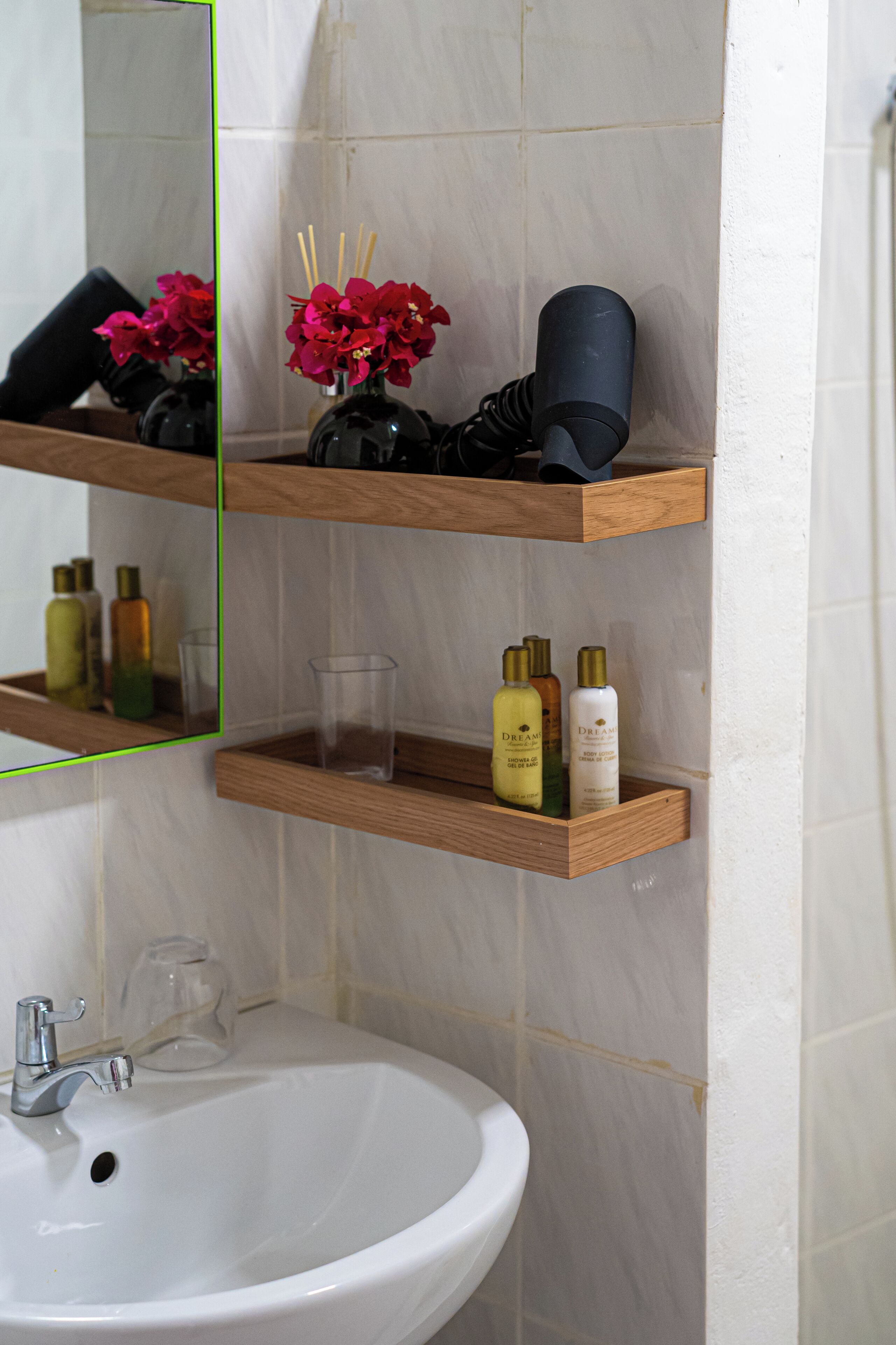 A bathroom with a white sink, wooden shelves above it, and a mirror reflecting the room.