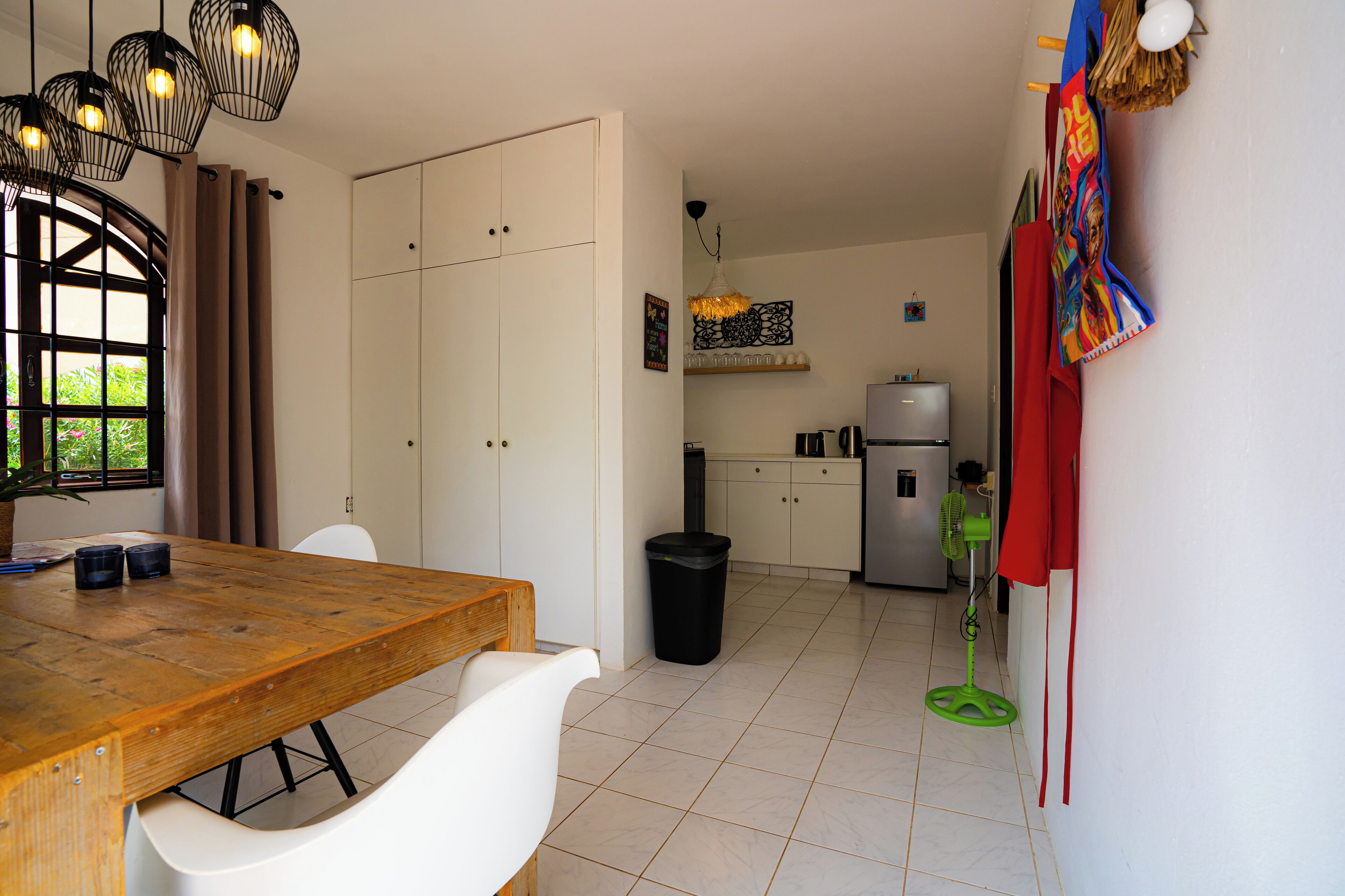 A modern kitchen with white cabinets, a wooden dining table, and a black trash bin.