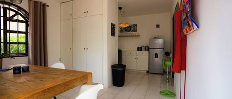 A modern kitchen with white cabinets, a wooden dining table, and a black trash bin.