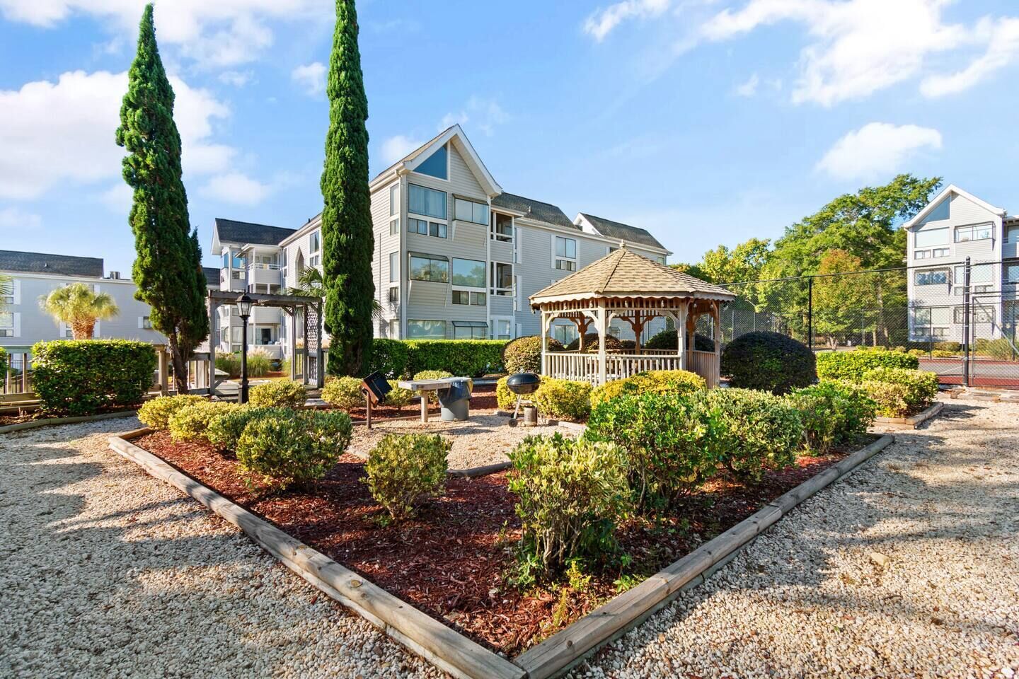 A residential area with a gazebo, well-maintained garden, and modern apartment buildings.
