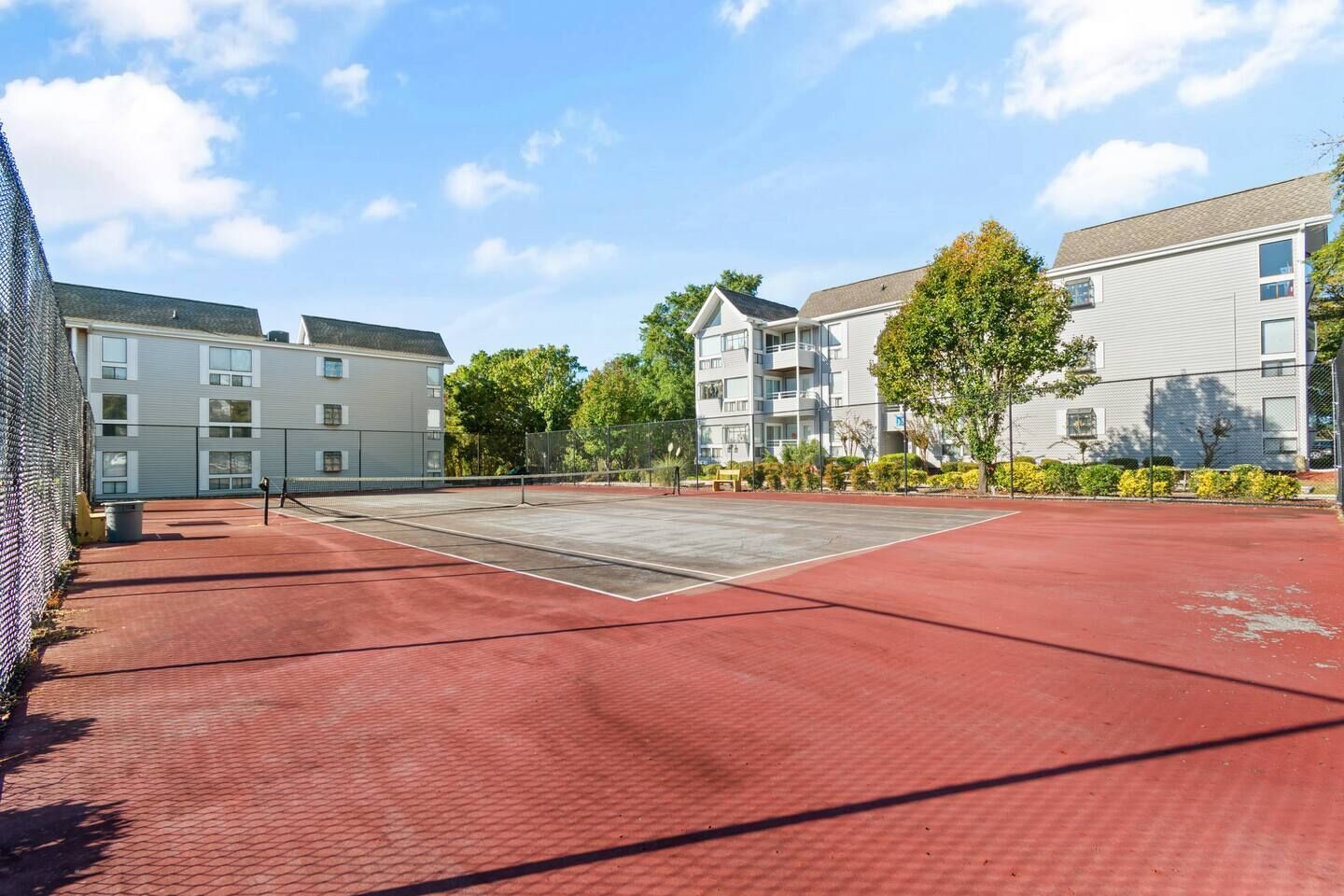 Ein Tennisplatz im Freien mit Netz, umgeben von Gebäuden und Bäumen.