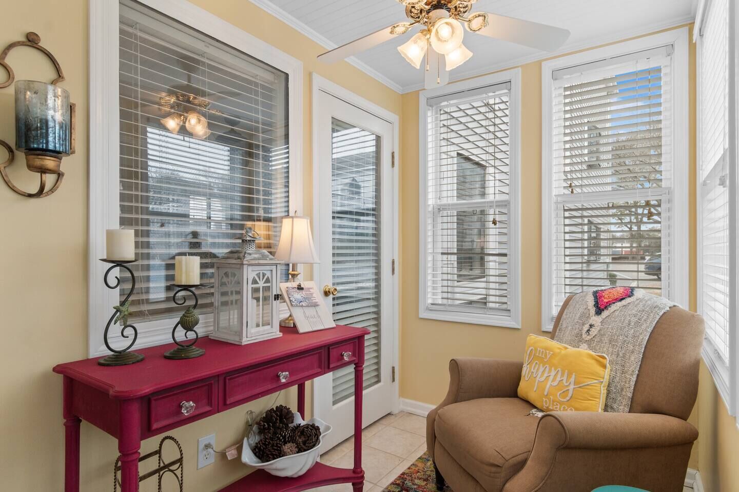 Une pièce avec une console rouge, un fauteuil marron et un ventilateur de plafond.
