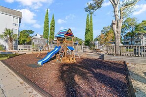 A playground with a slide and climbing structures, surrounded by trees and residential buildings. - Arcadian Dunes Coastal Retreat- pools, tennis, bar (Myrtle Beach)