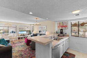 A modern kitchen with a central island, a dining area with a TV, and a living room with a sofa and a patterned rug. - Arcadian Dunes Coastal Retreat- pools, tennis, bar (Myrtle Beach)