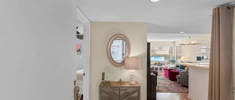 A hallway leading to a living area with a decorative console table, a mirror, and a lamp.