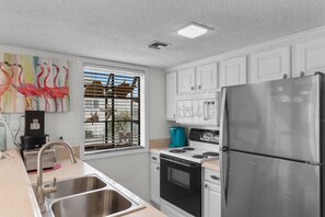 A kitchen with white cabinets, a stainless steel refrigerator, a stove, and a sink. - Arcadian Dunes Coastal Retreat- pools, tennis, bar (Myrtle Beach)