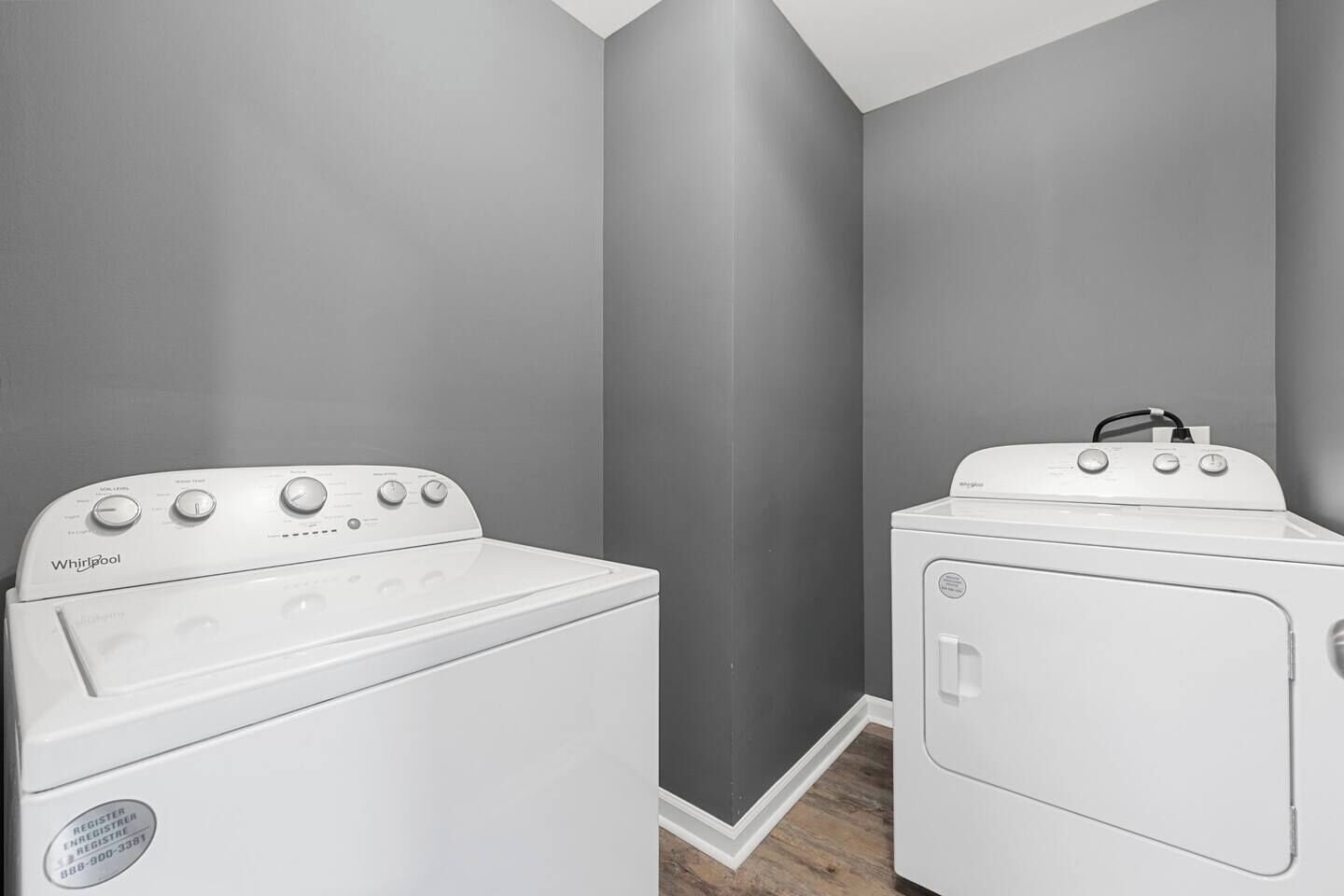 Una sala de lavandería con dos lavadoras y secadoras Whirlpool, paredes grises y piso de madera.