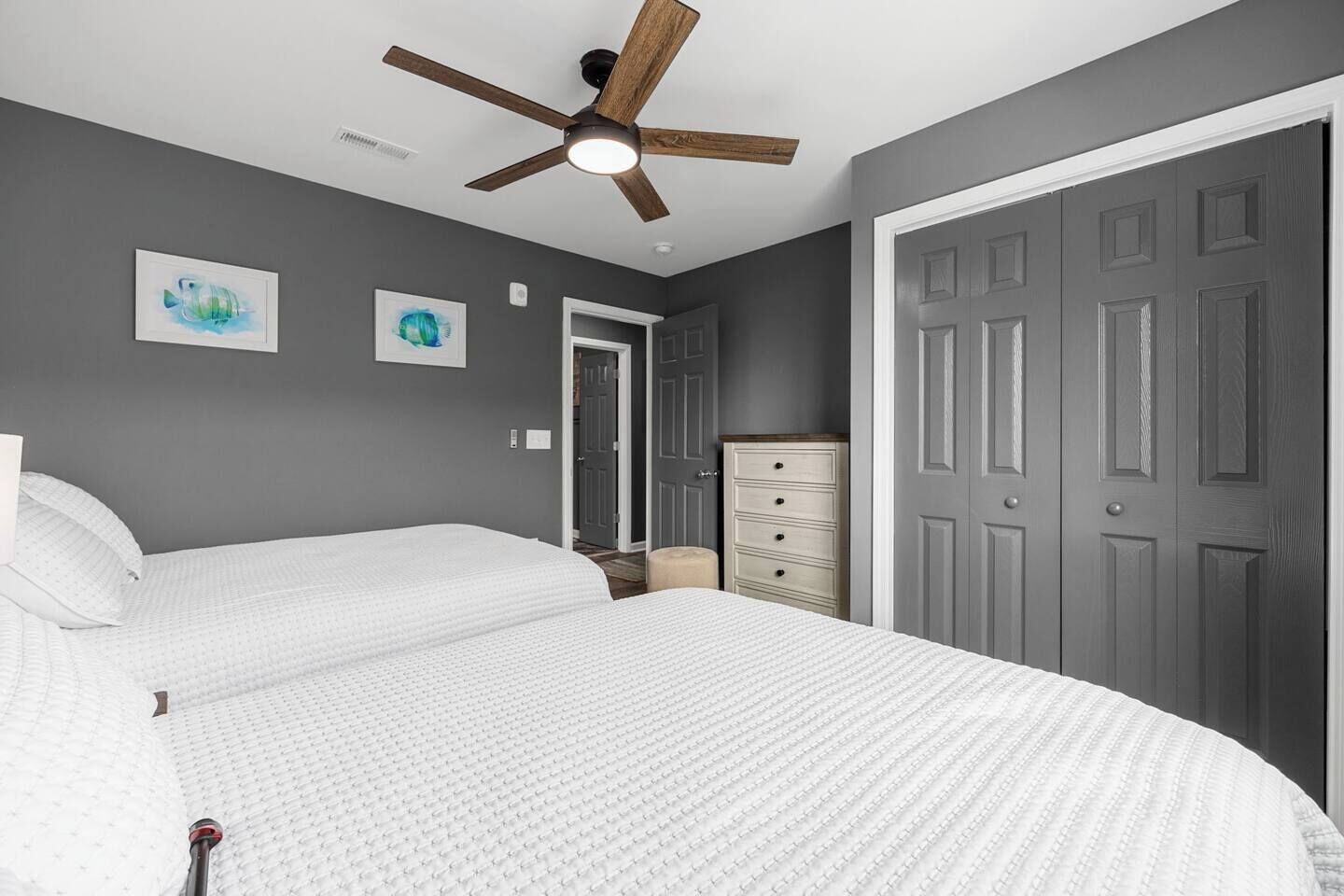 Een slaapkamer met een bed, een dressoir, een deur en een plafondventilator.