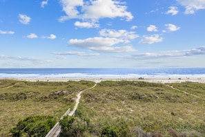 A coastal landscape with a sandy beach, grassy dunes, and a clear blue sky. - Totally Beachin' - Oceanfront, King Bed, Pool (North Myrtle Beach)