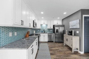 A modern kitchen with white cabinets, a stainless steel refrigerator, and a blue hexagonal backsplash. - Totally Beachin' - Oceanfront, King bed, Pool (North Myrtle Beach)