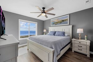 A bedroom with a bed, nightstands, a ceiling fan, a window with a view of the ocean, and a painting on the wall. - Totally Beachin' - Oceanfront, King bed, Pool (North Myrtle Beach)