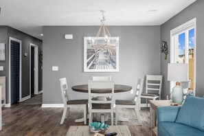 A dining area with a round table and chairs, a chandelier, and a framed picture on the wall. - Totally Beachin' - Oceanfront, King Bed, Pool (North Myrtle Beach)