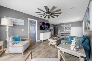 A modern living room with a wooden floor, a ceiling fan, a TV, and a sign that reads "my Beach Vacation Paradise". - Totally Beachin' - Oceanfront, King Bed, Pool (North Myrtle Beach)