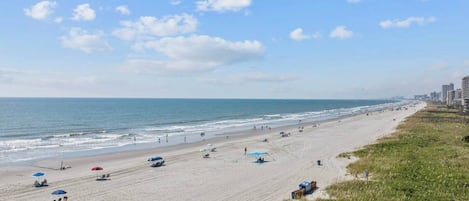 A beach with a long stretch of sand, some umbrellas, and a few people.