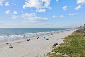 A beach with a long stretch of sand, some umbrellas, and a few people. - Totally Beachin' - Oceanfront, King bed, Pool (North Myrtle Beach)