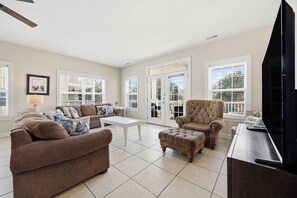 A living room with a sofa, armchair, ottoman, coffee table, and a television on a wooden cabinet. - 5 Bdrm Home w/ Epic gameroom, pool, put put, 7 bds (North Myrtle Beach)