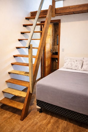 A bedroom with a wooden staircase, a bed with a patterned pillow, and a wooden wardrobe.