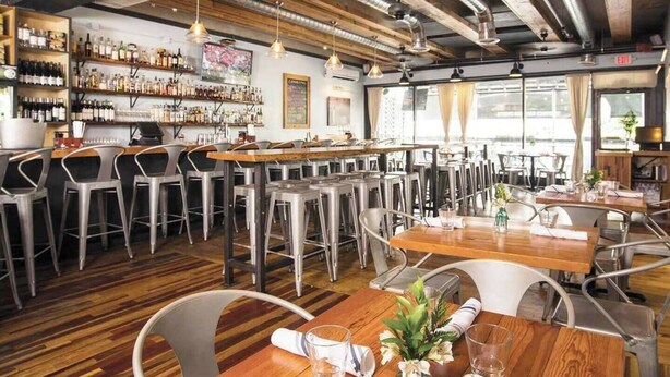 A restaurant with wooden tables and metal chairs, a bar area with shelves of bottles, and a view through large windows. - Updated, Wi-Fi, Coffee, Kitchen, Comfortable Bed (Athens)