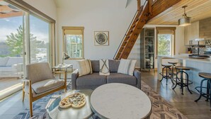 Un grand espace de vie comprenant un canapé, une table basse et des tabourets de bar, un escalier et un coin cuisine avec un bar.
