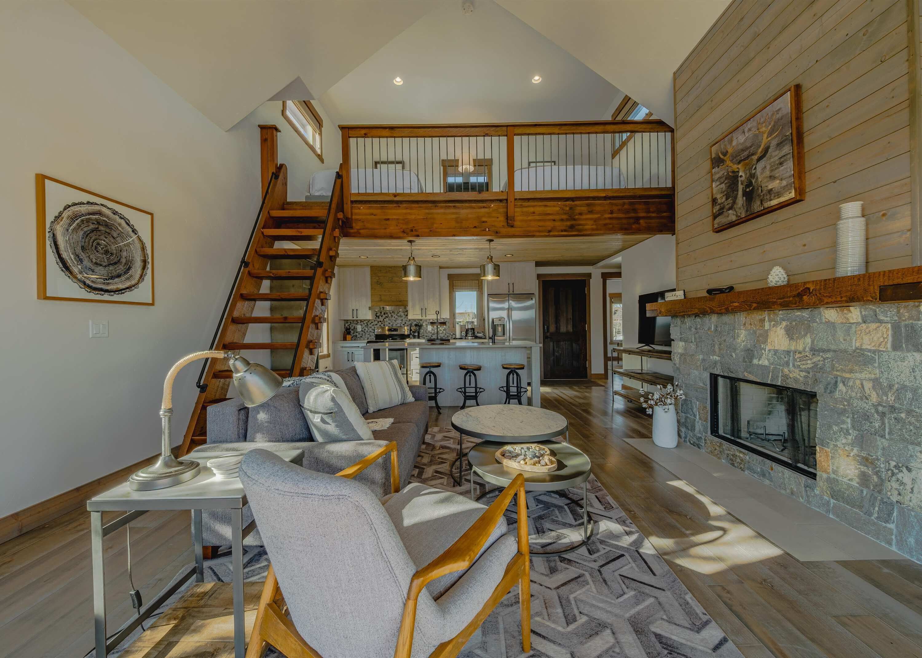 Un vaste espace de vie avec une chambre en mezzanine, une cheminée et une cuisine à l’arrière-plan.