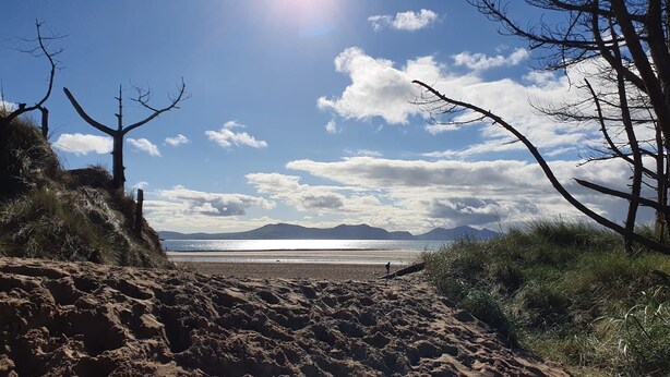 Une plage avec un ciel dégagé, des montagnes à l’horizon et une personne qui se promène.
