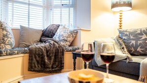 Un salon confortable avec un canapé, une table basse sur laquelle se trouvent un bol et un verre à vin, et une lampe.