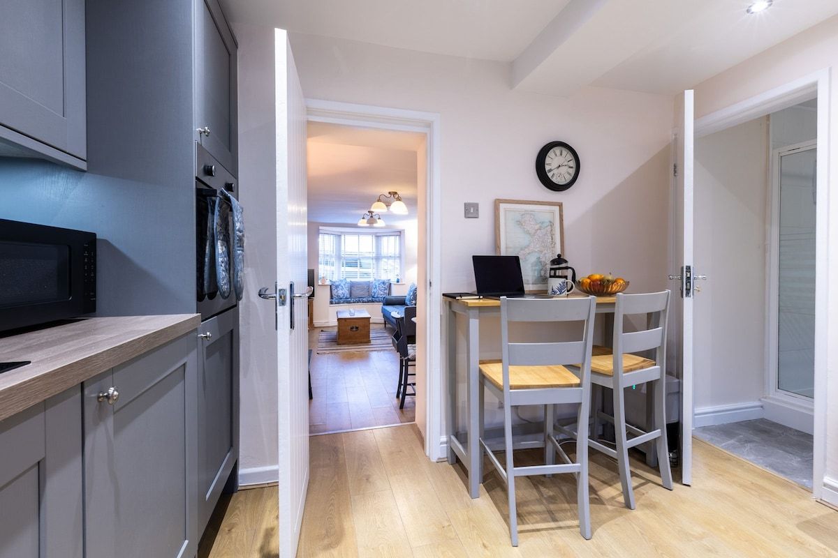 A kitchen with a microwave, oven, and cabinets, leading to a dining area with a table and chairs.