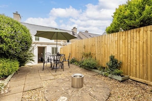 A patio with a table and chairs, a wooden fence, and a metal trash can.