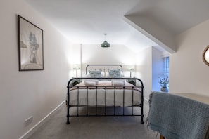 A bedroom with a bed, a bedside table, a lamp, a window, and a framed picture on the wall.